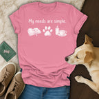 Pink t-shirt with "My needs are simple" and icons for book, paw print, candle, and tea.