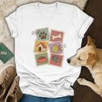 A white V-neck t-shirt featuring a colorful graphic of six vintage postage stamps with dog-related illustrations.