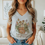 A woman wearing a gray V-neck t-shirt featuring a graphic of a puppy in a flowerpot with the text Homegrown Happiness.