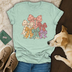 A mint green t-shirt featuring a stack of colorful bows patterned with paw prints, laid out with shoes and a small dog.