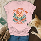 Pink t-shirt with a Corgi Garden Club graphic surrounded by flowers and garden tools, with a real dog, shoes, and jeans.