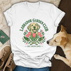 A white V-neck t-shirt features a green graphic with a Labrador retriever, pink tulips, and crossed garden trowels.