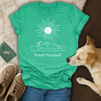 Green t-shirt with sun graphic and "Treat Yourself" text, lying next to a dog.