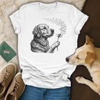 White t-shirt with a line drawing of a golden retriever blowing dandelion seeds that turn into paw prints.