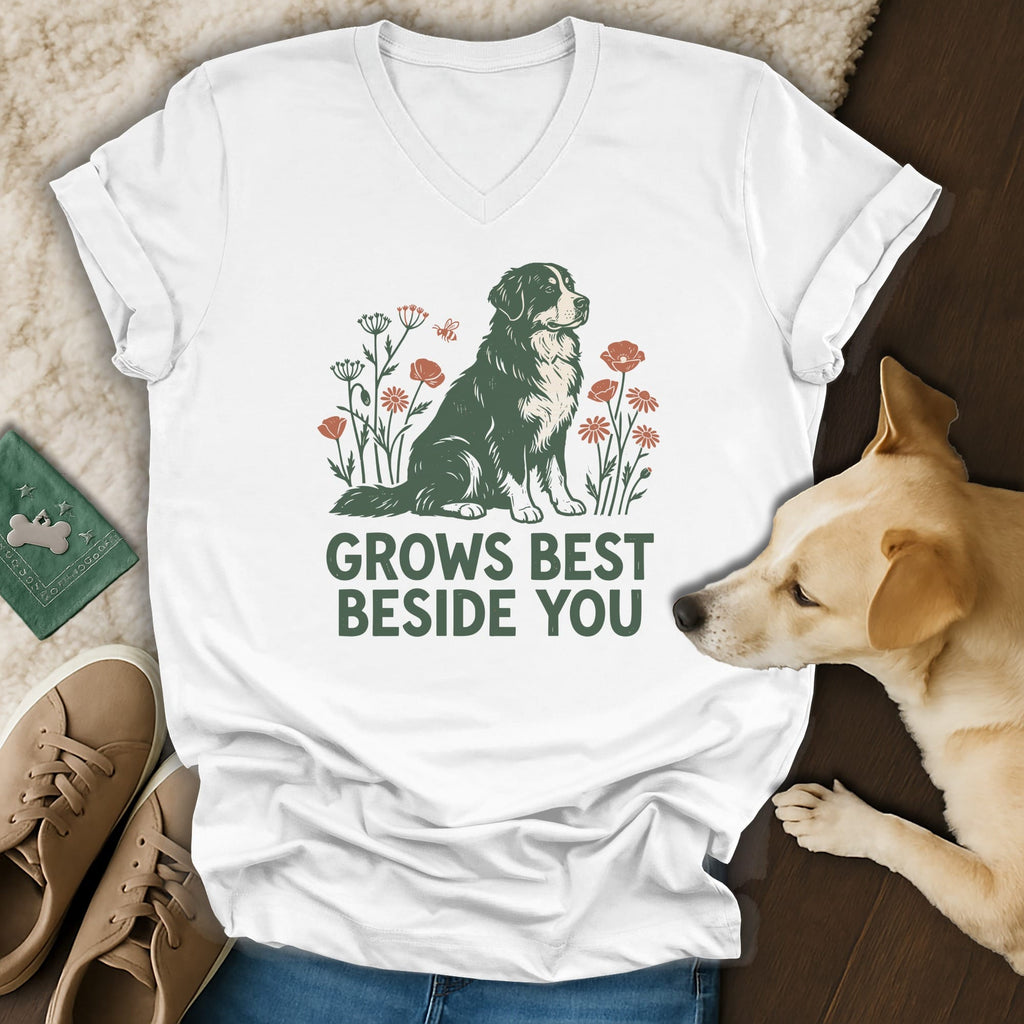 A white V-neck t-shirt featuring a green and red graphic of a Bernese Mountain Dog surrounded by flowers and the text GROWS BEST BESIDE YOU.